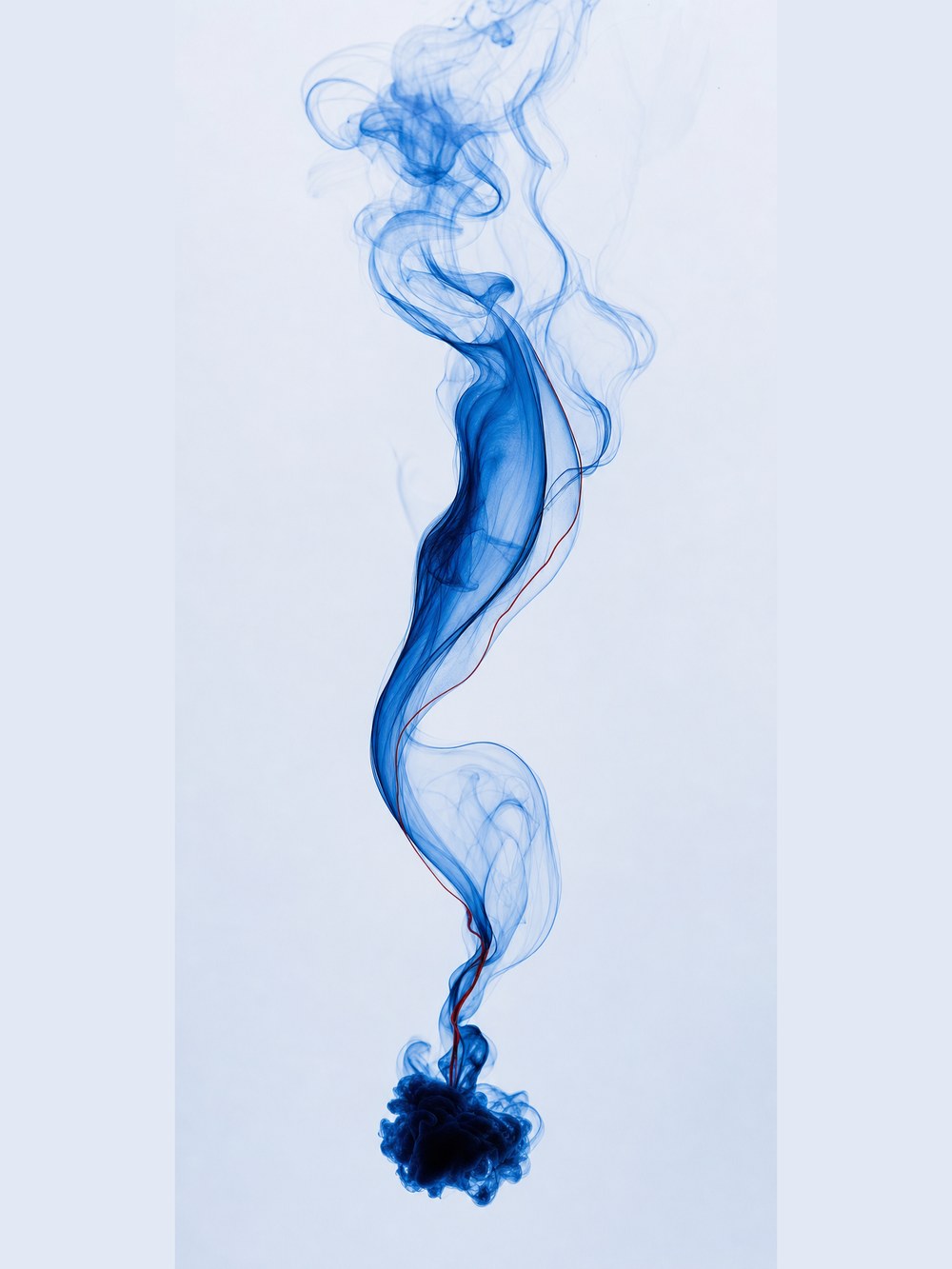 Cobalt ink unfurling through water in a slow river-like ribbon, gathering into one dense point at the bottom.